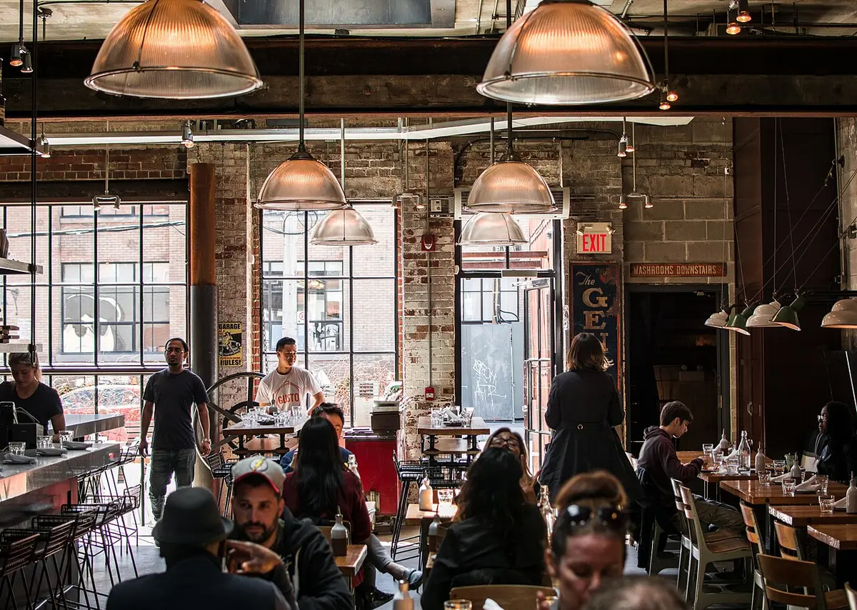 A busy dining room with guests at tables under hanging lamps