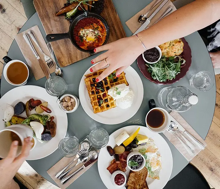 Friends reaching for plates of brunch on a shared table